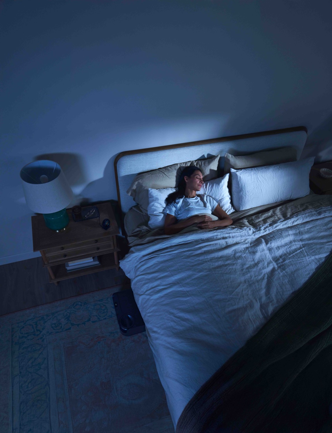 A woman sleeps calmly in cool blue light with the ChiliPad control unit beside the bed.