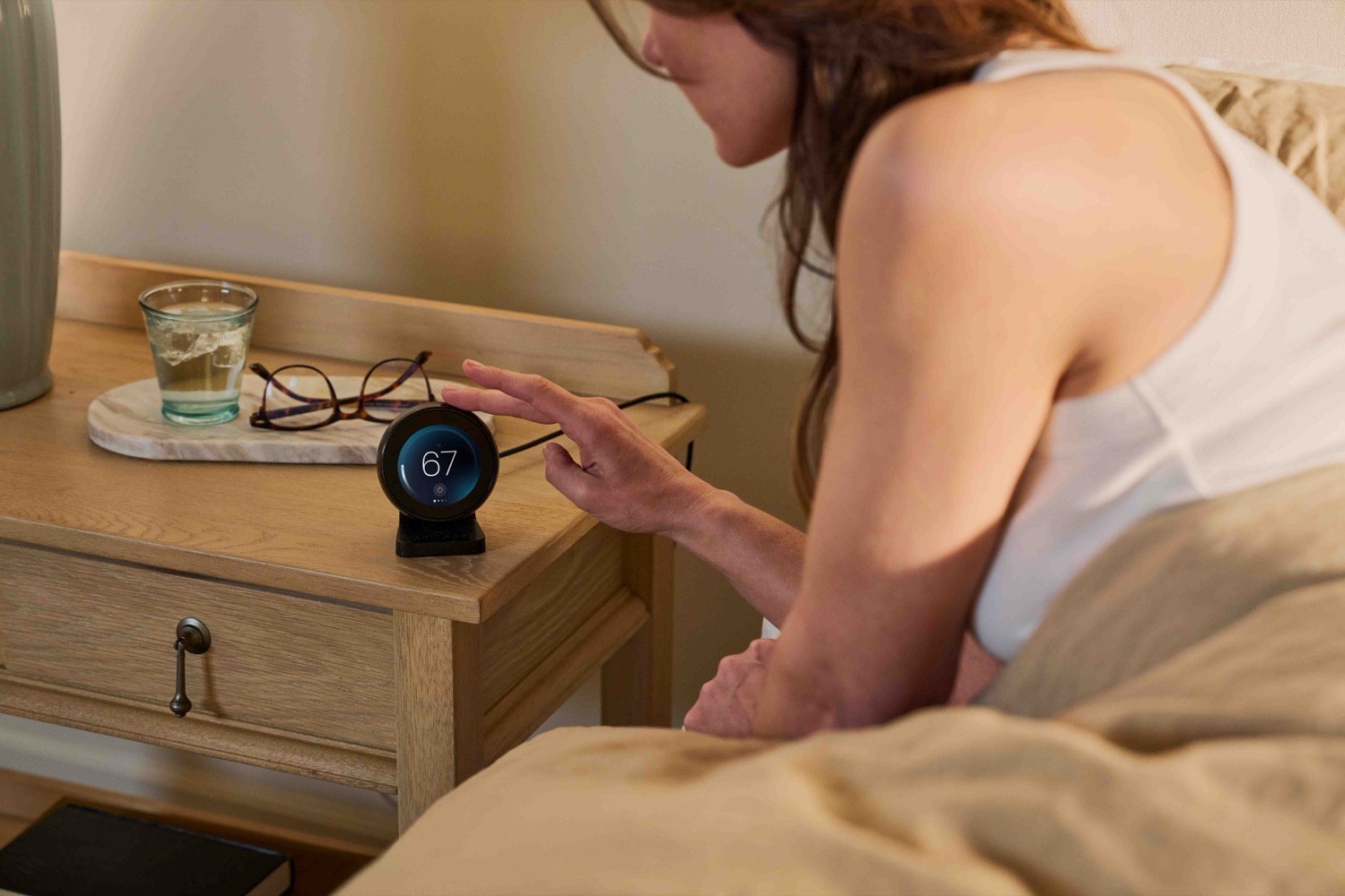 Woman setting the bedside control to 67 degrees.